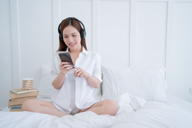 beauty-asian-female-white-dress-long-hair-wear-headphone-use-type-search-smartphone-white-bed-with-clam-cheerful-white-bedroom-interior-background