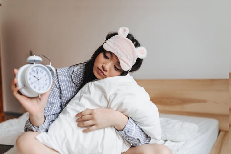 woman-pink-sleeping-mask-is-hugging-pillow-looking-alarm-clock-with-sadness